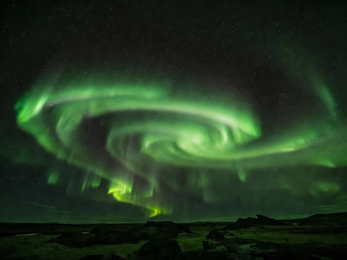 Green aurora borealis glowing over snow-capped Icelandic mountain peaks