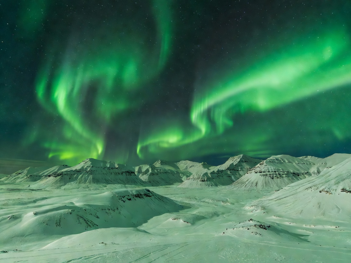 Vibrant green aurora borealis arcing over snowy mountain landscape in Iceland